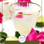 A glass of elderflower cocktail garnished with a pink rose petal, surrounded by a cut lime, rose flower, and another similar drink in the background.