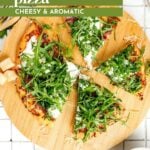 A sliced burrata pizza topped with fresh arugula and cheese sits on a wooden board, surrounded by scattered cheese and pizza ingredients.