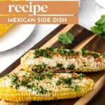 Two ears of elote corn topped with cheese, chili powder, and chopped herbs are served on a wooden board, with text overlay describing the dish as a Mexican side.