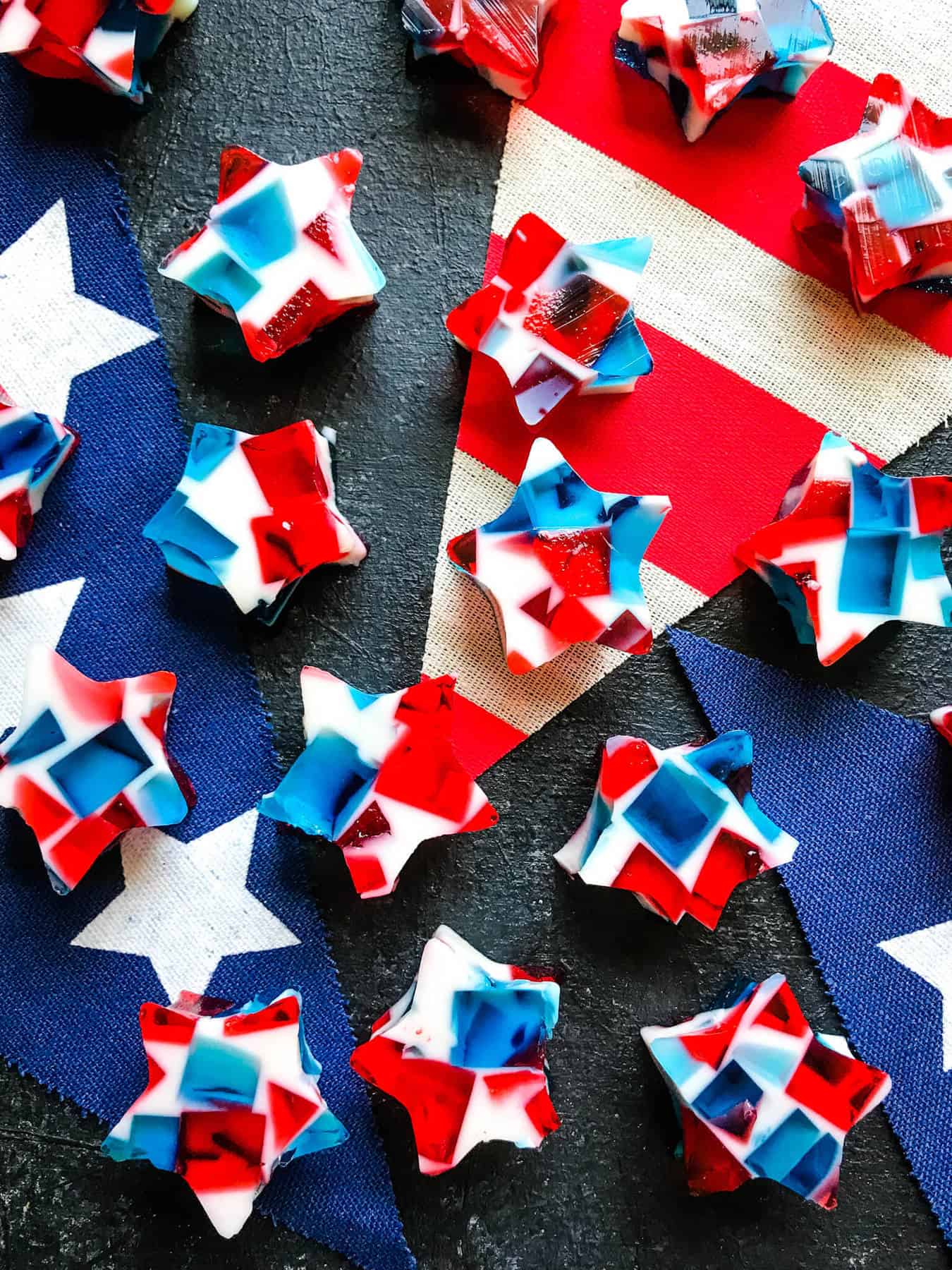 Red, white, and blue star-shaped jello pieces are arranged on a dark surface with a red, white, and blue star-patterned fabric banner underneath.