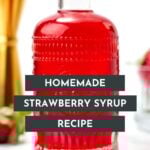 A clear glass bottle filled with bright red strawberry syrup sits on a white surface, with a gold jigger and strawberries blurred in the background. Text overlay reads "Homemade Strawberry Syrup Recipe.