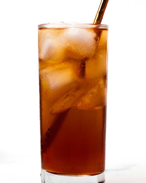 A tall glass filled with iced coffee and a metal straw, with a few coffee beans placed on the surface nearby.