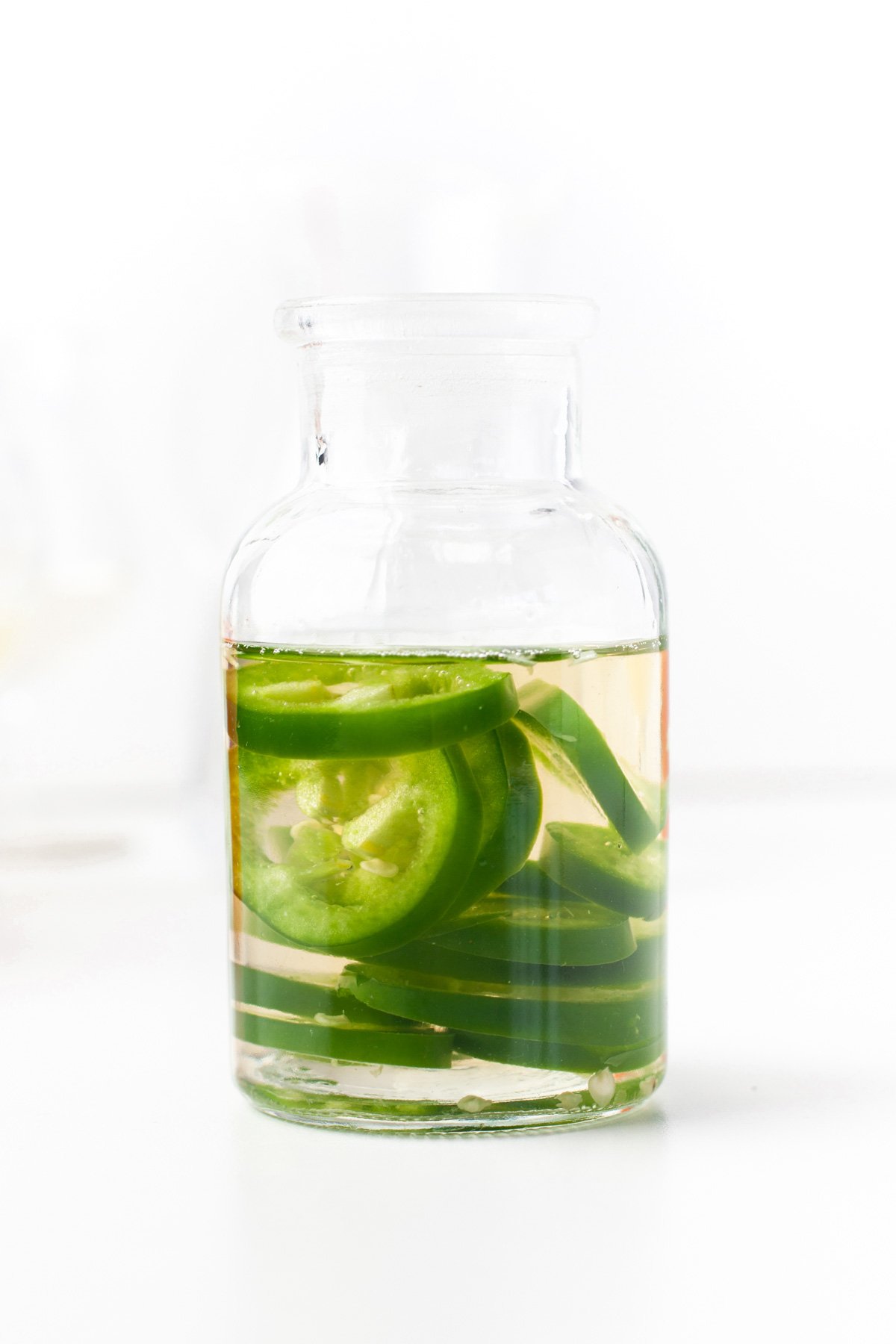 A clear glass jar filled with liquid and several slices of green jalapeño peppers.
