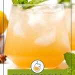 A glass of bourbon smash cocktail with ice and mint garnish, set on a white surface with lemon and mint leaves nearby.