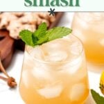 A glass of whiskey smash cocktail with ice and mint garnish, next to another glass and a cutting board with ginger.