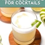 A glass of a cocktail with a foamy top and a lime garnish sits on a wooden coaster, accompanied by text promoting aquafaba as a vegan egg white alternative for cocktails.