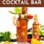 A Bloody Mary cocktail garnished with shrimp, bacon, olives, vegetables, and cheese, with a bottle of hot sauce and fresh ingredients in the background. Text reads "How to set up a Bloody Mary Cocktail Bar.