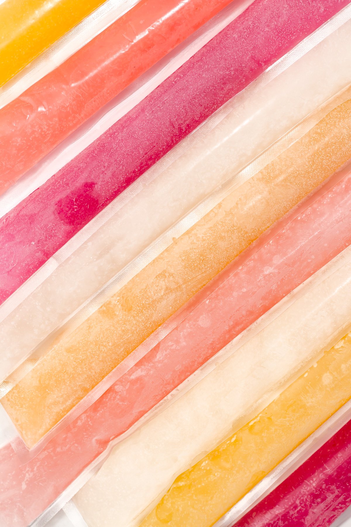 A close-up view of assorted colorful ice pops in plastic sleeves arranged in diagonal rows.