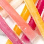Assorted colorful ice pops in plastic sleeves are arranged in an overlapping pattern on a white surface.