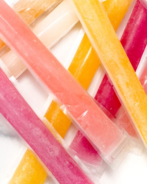 Assorted colorful ice pops in plastic sleeves are arranged in an overlapping pattern on a white surface.