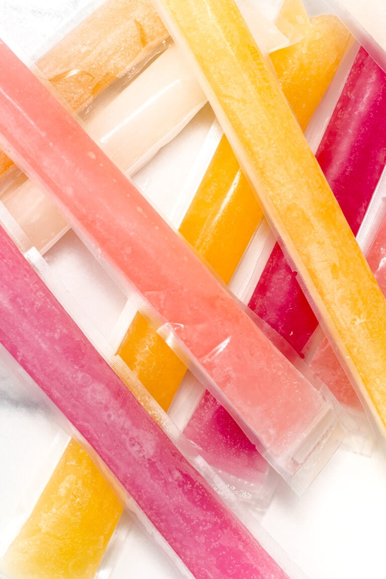 Assorted colorful ice pops in plastic sleeves are arranged in an overlapping pattern on a white surface.