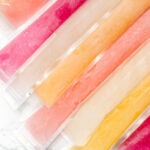 Assorted freeze pops in clear plastic sleeves are arranged side by side on a white surface.