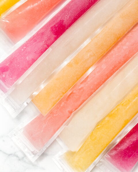 Assorted freeze pops in clear plastic sleeves are arranged side by side on a white surface.