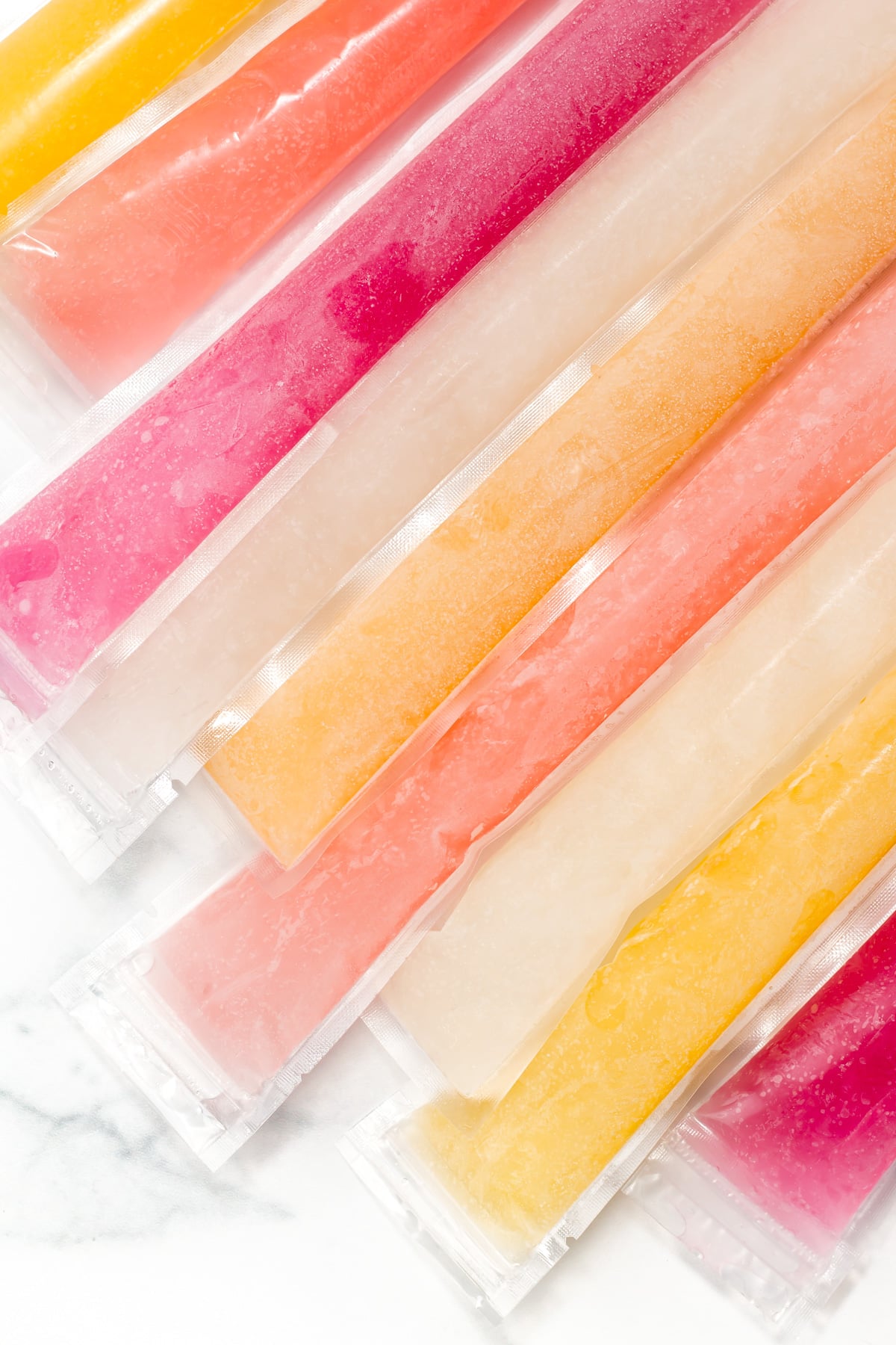 Assorted freeze pops in clear plastic sleeves are arranged side by side on a white surface.
