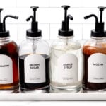 Four labeled pump bottles of coffee syrup—cinnamon, brown sugar, simple syrup, and mocha—are neatly arranged on a white tray against a tiled background, perfect for creating the ultimate coffee experience at your home Coffee Bar.