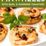 Close-up of Puff Pastry Pinwheels filled with herbs and sun-dried tomatoes, served on a white plate and garnished with fresh basil leaves.