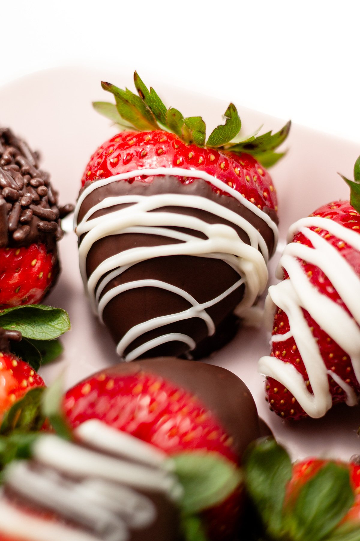 A chocolate-covered strawberry drizzled with white chocolate sits on a plate with other decorated strawberries.