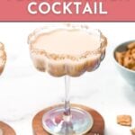 A creamy cocktail in a sugar-rimmed glass sits on a wooden coaster with cinnamon toast cereal pieces nearby; text reads “Cinnamon Toast Crunch Cocktail.”.