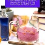 A glass mug with a pink cocktail is on a table next to a blue liquid in a small bottle, books, and a cocktail stirrer. Text reads "25 Halloween Cocktails.