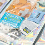 A care kit with hangover relief tablets, mint candies, bandages, a packet of wipes, a fabric scrunchie, and an information card displayed on a holographic surface.