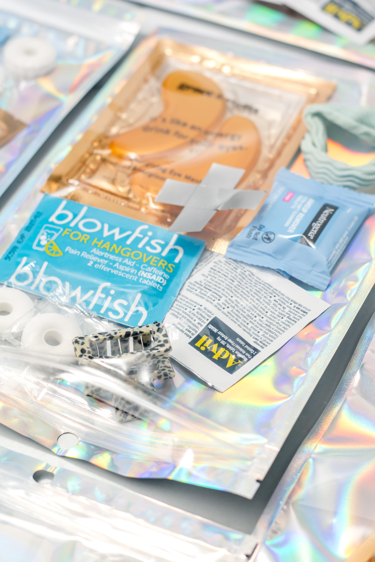 A care kit with hangover relief tablets, mint candies, bandages, a packet of wipes, a fabric scrunchie, and an information card displayed on a holographic surface.