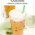 A glass of iced Irish coffee topped with whipped cream and a green polka dot straw, with a green striped cloth and another glass in the background.