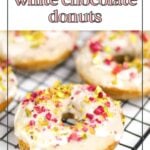 Four raspberry white chocolate donuts with white icing and colorful sprinkles are cooling on a black wire rack.