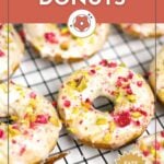 Iced raspberry donuts topped with crushed nuts and fruit pieces, arranged on a cooling rack; promotional text and website branding are included.