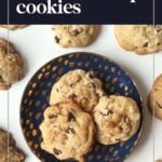 A blue plate with three chocolate chip cookies sits on a white surface surrounded by more cookies. Text reads "bourbon chocolate chip cookies.