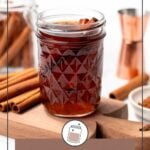 A glass jar of cinnamon syrup sits on a wooden board surrounded by cinnamon sticks and copper bar tools. Text reads "Cinnamon Syrup" and "Easy to Make.