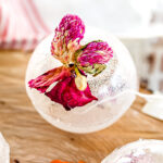 A clear ice sphere with a pink and purple dried flower frozen inside sits on a wooden surface.
