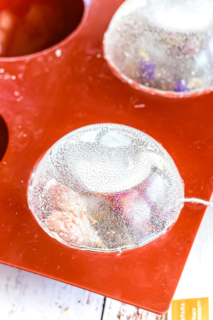 A clear chocolate half-sphere mold containing a shiny, smooth dome sits in a red silicone mold tray on a white surface.