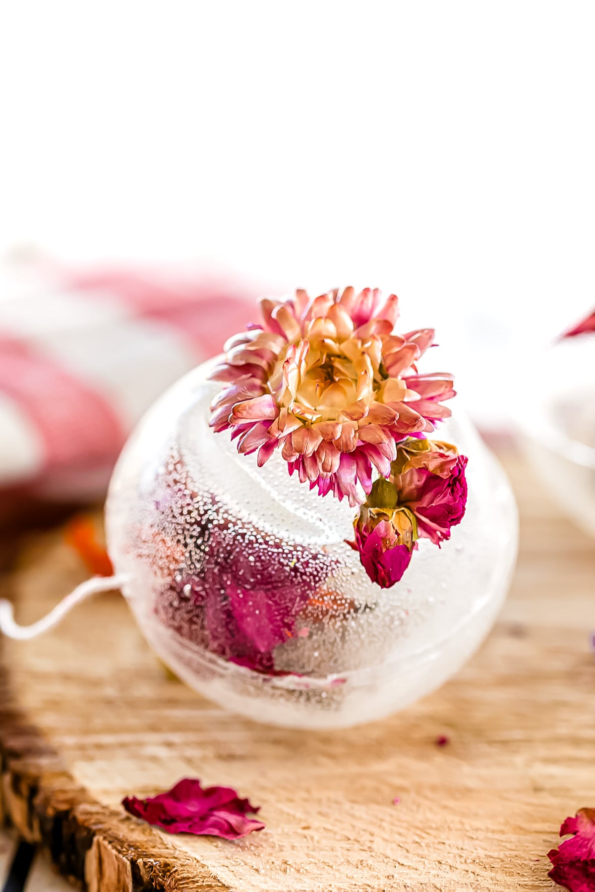 A clear glass ornament with dried pink and orange flowers inside and on top, resting on a wooden surface.