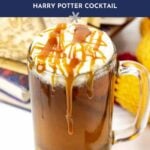 A glass mug of homemade butterbeer topped with foam and caramel drizzle, with a knitted scarf and books in the background. Text reads: "homemade butterbeer, Harry Potter cocktail.