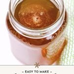 A mason jar filled with honey whiskey sits on a surface, with a green textured cloth nearby. Text reads: "Easy to make homemade honey whiskey.