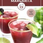 Two glasses of dark red spicy jalapeño blackberry margarita with ice, garnished with lime and blackberries, sit on a white surface with lime halves and jalapeños nearby.