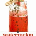 A glass of pink watermelon mimosa with gold star patterns, garnished with a watermelon wedge and a sprig of herbs. Text reads "watermelon mimosas—sweet & sparkling drink.