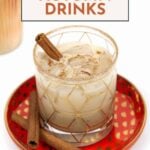 Glass of creamy autumn drink with ice and cinnamon sticks on a red polka dot plate, labeled "23 Autumn Drinks"—perfect inspiration for cozy fall cocktails.