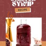 A clear glass bottle filled with dark red blood orange syrup sits on a white surface next to a sliced blood orange and a gold jigger.