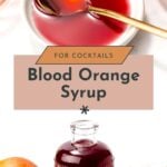 A bottle and bowl of deep red blood orange syrup with a spoon, fresh blood oranges, and glassware arranged on a white surface.