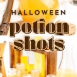 Round glass bottles filled with orange liquid are arranged on a table with text that reads “Halloween potion shots.”.