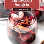 A glass of dark sangria with orange slices, star anise, and lychee “eyeballs,” labeled as a Halloween sangria recipe.