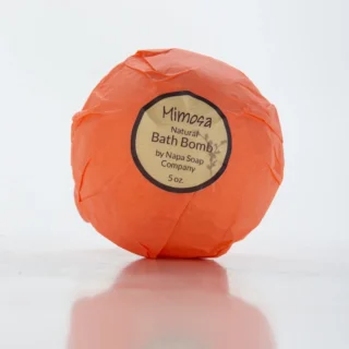 An orange-wrapped bath bomb labeled "Mimosa Natural Bath Bomb by Napa Soap Company, 5 oz." on a plain white background.