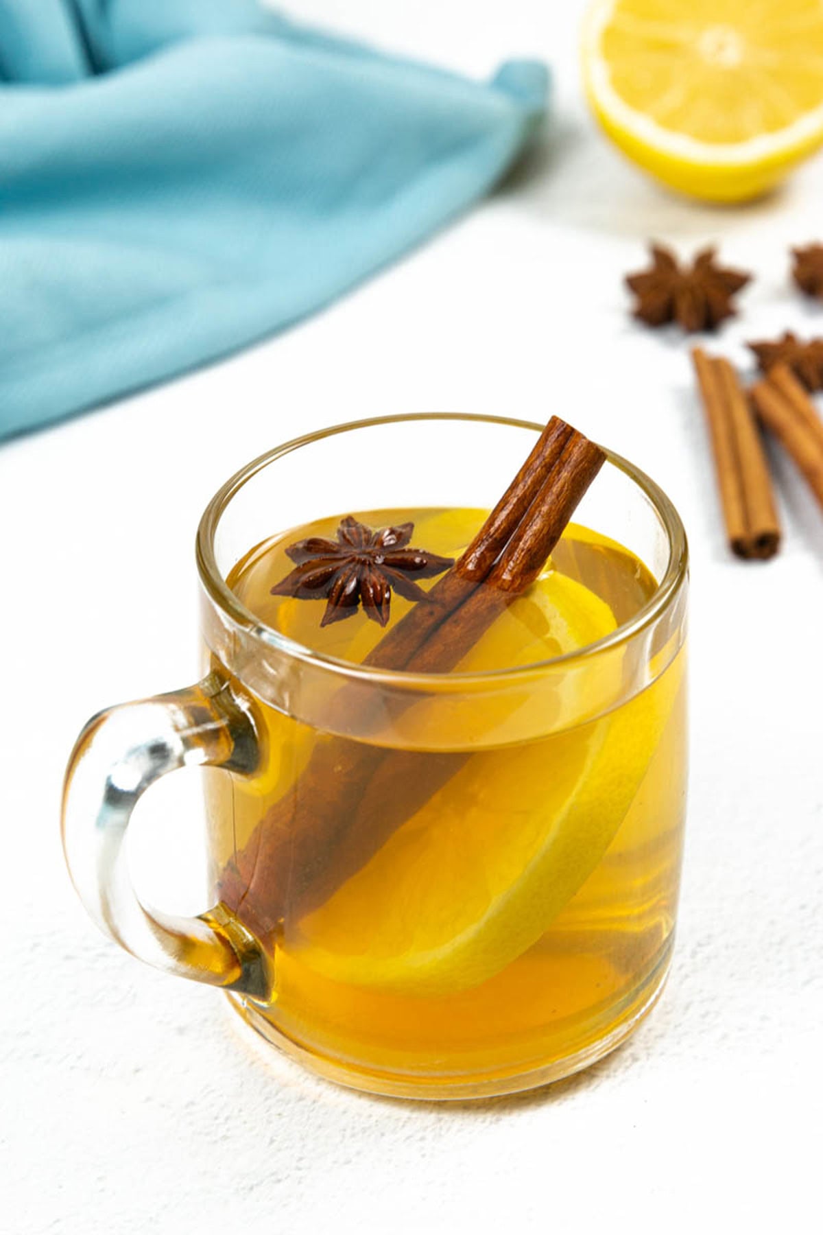 A glass mug of tea with a lemon slice, cinnamon stick, and star anise on a white surface evokes the comforting flavors often found in bourbon cocktails.