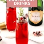 A glass of red cranberry drink garnished with sugared cranberries and rosemary sits in front of a champagne bottle and cocktail shaker.