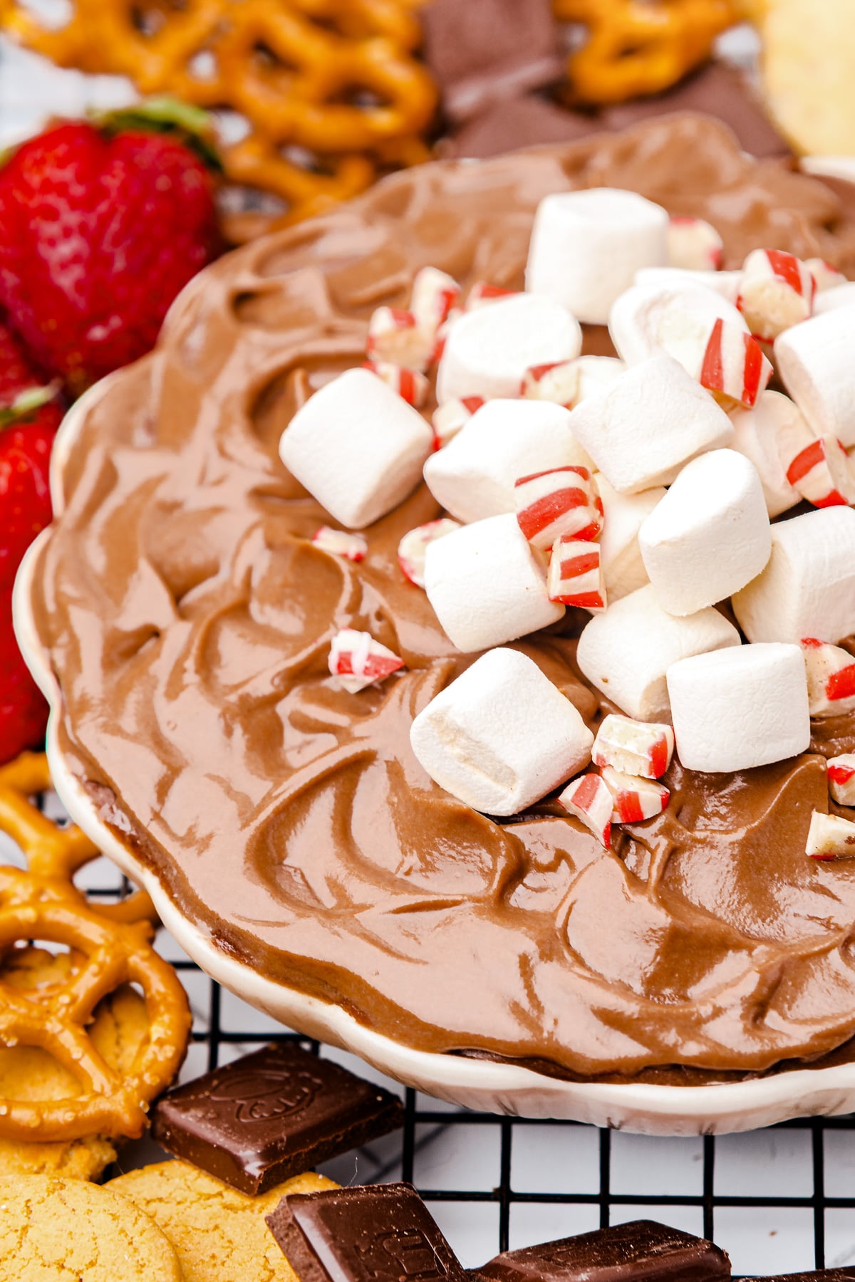 A bowl of chocolate mousse dip topped with mini marshmallows and crushed peppermint, surrounded by pretzels, strawberries, cookies, and chocolate pieces.
