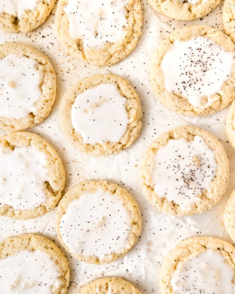 Iced sugar cookies arranged on parchment paper, topped with white glaze and sprinkled with black specks.