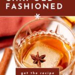 A glass of chai old-fashioned cocktail with star anise and a large ice cube sits beside a cinnamon stick, with text promoting the recipe.