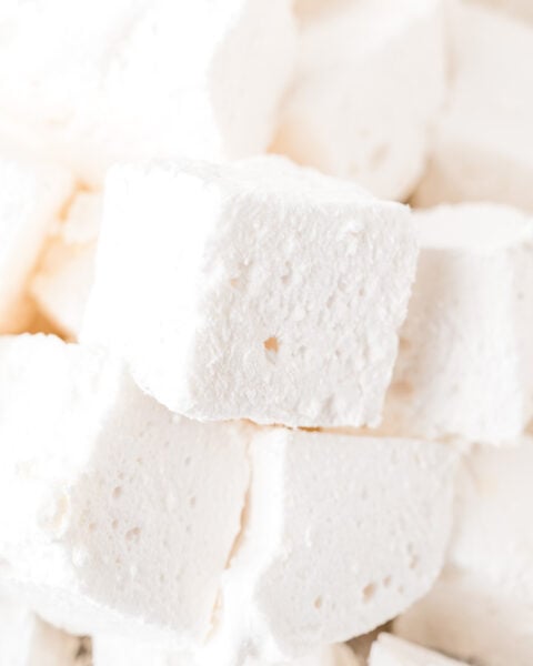 Close-up of several white, square marshmallows stacked together, showing their soft, fluffy texture and small air holes.