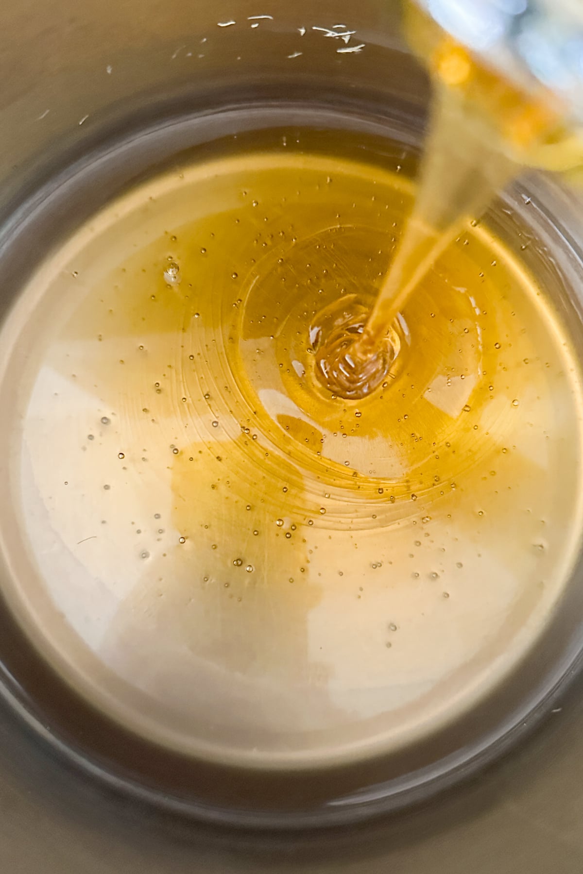 Golden honey ginger syrup being poured into a bowl, creating swirls and bubbles on the smooth surface.